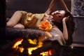 A girl in sexy silk pajamas lies on a bed against a blazing fire