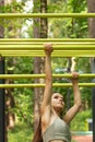 Girl shakes her arm muscles, a teenager pulls herself up on a sports trainer on the street, summer activities for youth