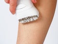 A girl shaves her leg with an electric epilator on a white background.