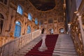 A girl in a shiny dress standing on the steps of a luxurious historical palace staircase.