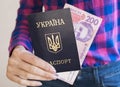 A girl in a shirt and jeans holds in her hand a Ukrainian passport and a banknote of 200 hryvnias