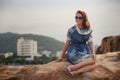 girl in short grey frock sits on rock shows legs against city