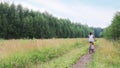 Girl in shorts rides bicycle in summer green forest, back view