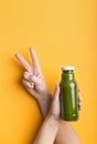 Girl showing v sign and advertising Glass bottle with green smoothie