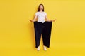 Girl showing weight loss, astonished girl with opened mouth, lady in white t shirt wearing old black pants in huge size, standing Royalty Free Stock Photo