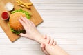 The girl shows willpower by holding with her left hand, her right hand that reaches for a hamburger. Diet and healthy nutrition,