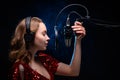 A girl singer sings into a microphone, with a spectacular background, vocals, a recording studio, recording a track. On a black Royalty Free Stock Photo