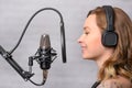 Girl sings into a microphone, in headphones in a studio. Producing and creating songs, music, recording a track. Writing an album