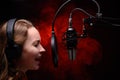 Girl sings in a red dress and red backlight. Microphone in a recording studio. Effective background. Vocal. Vocal schools and Royalty Free Stock Photo