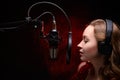 Girl sings in a red dress and red backlight. Microphone in a recording studio. Effective background. Vocal. Vocal schools and Royalty Free Stock Photo