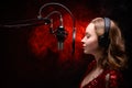 Girl sings in a red dress and red backlight. Microphone in a recording studio. Effective background. Vocal. Vocal schools and Royalty Free Stock Photo