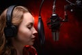 Girl sings in a red dress and red backlight. Microphone in a recording studio. Effective background. Vocal. Vocal schools and Royalty Free Stock Photo