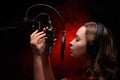 Girl sings in a red dress and red backlight. Microphone in a recording studio. Effective background. Vocal. Vocal schools and Royalty Free Stock Photo