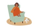 Girl siting on chair at home with his knees pulled up to his ches. Pet cat lying at her feet on rug. Domestic Cat