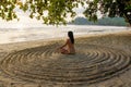 The girl sits back on the sandy beach in the center of an impromptu circle and meditates
