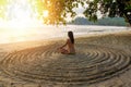 The girl sits back on the sandy beach in the center of an impromptu circle and meditates