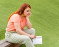 A girl sits on a bench. Sad beautiful ginger woman holds a white paper bag in her hand. Female holding packet with food Royalty Free Stock Photo