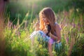 A girl sits in a blooming field with a beautiful tricolor kitten. Blooming sage