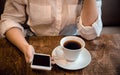 Girl sits in a cafe and holds a cup of tea and a phone in her hands, waiting for a call
