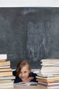 Girl sits in classroom among heap of school lector. Satisfied schoolgirl. School board in the background Royalty Free Stock Photo
