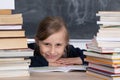 Girl sits in classroom among heap of school lector. Satisfied schoolgirl. School board in the background Royalty Free Stock Photo