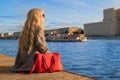 The girl sits at the dock and looks into the distance. Warm autumn weather by the river. Royalty Free Stock Photo