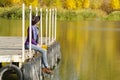 Girl sits on a dock near the water in a hat and with leaves in h Royalty Free Stock Photo