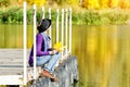 Girl sits on a dock near the water in a hat and with leaves in her hands. Sunny day Royalty Free Stock Photo