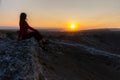 The girl sits on the edge of the cliff and looks at the sun Royalty Free Stock Photo