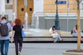 The girl sits at the fountain and looks at the smartphone screen.