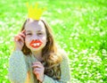 Girl sits on grass at grassplot, green background. Child posing with cardboard smiling lips and crown for photo session Royalty Free Stock Photo