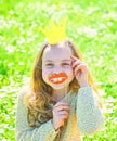 Girl sits on grass at grassplot, green background. Child posing with cardboard smiling lips and crown for photo session