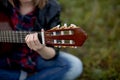 A girl sits on the grass with a guitar playing, putting her hand