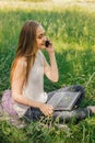 girl sits on the grass and works at a laptop. talking on the phone. freelance. selfeducation. the concept of remote