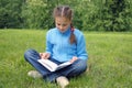 Girl sits on green field and reads book