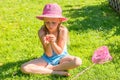 A girl sits on a green lawn in a pink hat with a day butterfly caught by a baby net. Royalty Free Stock Photo