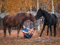 The girl sits on the ground and holds two horses by the reins. Autumn photography