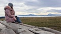 A girl sits with her back on wooden logs high in the Carpathians in cold autumn weather and enjoys a beautiful view of the Royalty Free Stock Photo