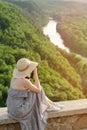 Girl sits on hill and takes pictures against the background of a forest and meandering river Royalty Free Stock Photo