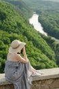 Girl sits on hill and takes pictures against the background of a forest and meandering river Royalty Free Stock Photo