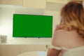 The girl sits at home in the evening on the couch in front of the TV. A woman looks at the news after work. Green monitor screen