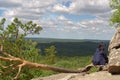 The girl sits on a horizontally growing pine tree on the edge of a cliff