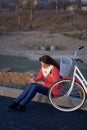 The girl sits next to a parked bike. Watching something on the phone. Rest on the spring cycle Royalty Free Stock Photo