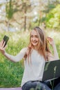 girl sits outdoors and works at a laptop. makes a selfie on the phone. freelance. selfeducation. the concept of remote