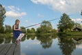 A girl sits on a pole of a boardwalk at a lake with a fishing r Royalty Free Stock Photo