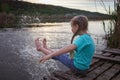 Girl sits on pontoon bridge at lake and enjoys warm sunny evening, happy summertime, countryside Royalty Free Stock Photo