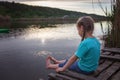 Girl sits on pontoon bridge at lake and enjoys warm sunny evening, happy summertime, countryside Royalty Free Stock Photo