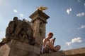 The girl sits on the railing of the stairs on the bridge of Alexander the Third and looks into the smartphone