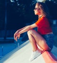 A girl sits on the ramp skate park in the rays of warm sun. Outdoor, summer. Warm color.