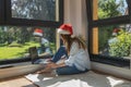 A girl sits in a room on the floor in front of a laptop in a Santa hat and makes online purchases or a video call Royalty Free Stock Photo